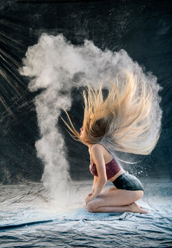 Woman with long hair kneels in a dust cloud, creating dynamic movement against a dark backdrop. WA, USA
