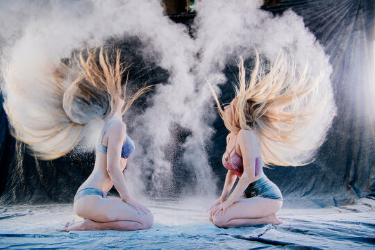 Two women toss their hair, creating dramatic flour clouds against a dark background. WA, USA