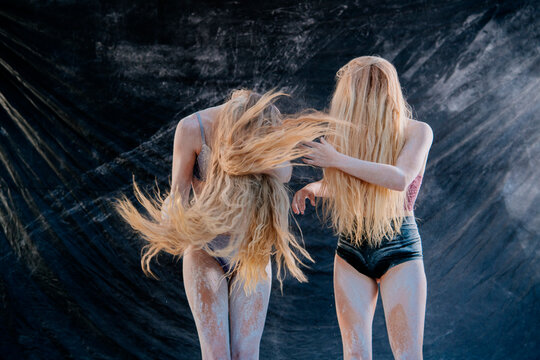 Two women with long blonde hair perform expressive dance on dark draped fabric backdrop. WA, USA
