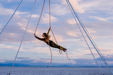 Aerial performer in colorful suit gracefully swings over a calm sea at sunset. WA, USA