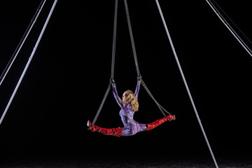 Aerial performer in a bodysuit doing splits on chains amid a dark backdrop. WA, USA