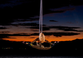 Aerial performer in a gold costume suspended against a vibrant sunset sky. WA, USA