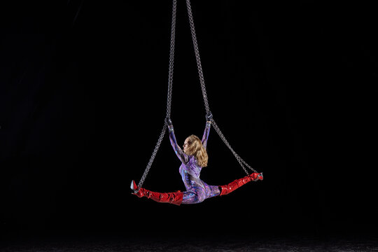 Aerial performer in a bodysuit doing splits on chains amid a dark backdrop. WA, USA