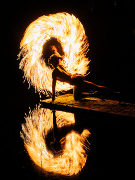 Silhouette of a dancer spinning fire poi, creating a fiery halo effect and vivid reflection. WA, USA