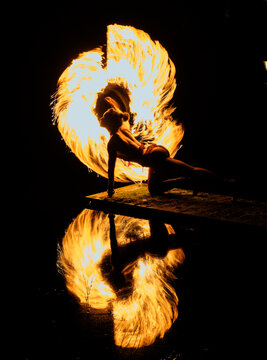 Silhouette of a dancer with fiery trails and reflection over water in motion. WA, USA