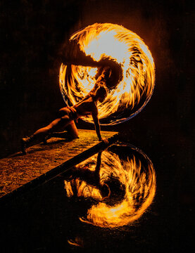 A performer spins fire, creating a dramatic circle reflection in the water at night. WA, USA