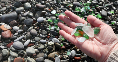 Woman put glass sea pebbles of different colours on shore, beach. Nature and ecology. Background for design.