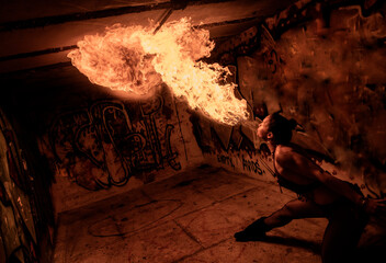 Fire breather performs in a graffiti-covered urban setting with dramatic lighting. WA, USA