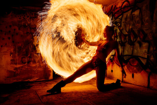 Performer twirls a flaming hoop in a graffiti-covered urban setting at night. WA, USA