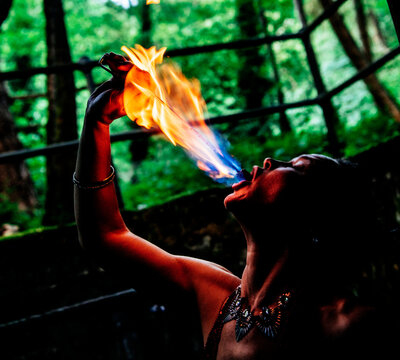Performer breathes fire in a forest setting, surrounded by lush greenery. WA, USA