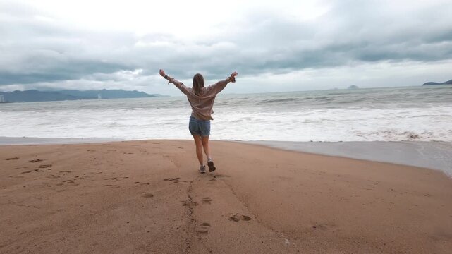 young woman enjoys the deserted sea. A girl in a shirt and short shorts enjoys the boundless sea and the sea breeze and lift hands up.