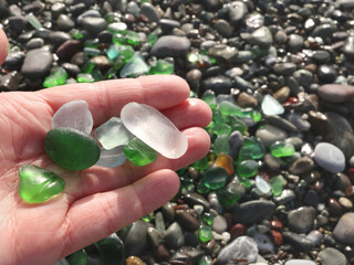 Woman put glass sea pebbles of different colours on shore, beach. Nature and ecology. Background for design.