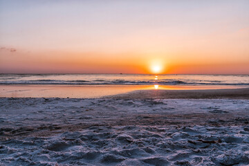 Obraz premium The beach is empty and the sun is setting. The sky is a beautiful mix of orange and pink hues