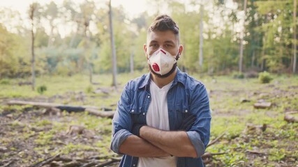 Medium view of Caucasian male volunteer wearing protective mask. Bearded man crossing arms confidently. Standing in forest clearing. Preparing environmental work. Nature conservation concept.