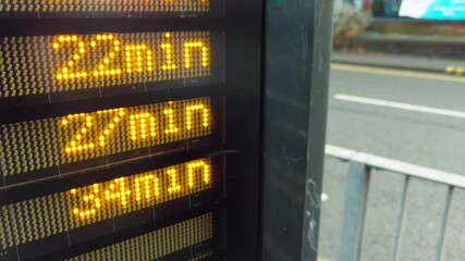 Bus stop digital display counting down arrival time in urban street. LED numbers changing while waiting time decreasing for public transport. City timetable board updating minutes during daily commute