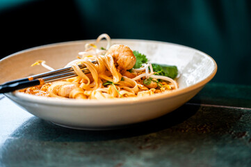 Close-up of a delicious, spicy prawn and chicken curry laksa noodle soup in a white bowl, with chopsticks lifting a serving, focus on shrimp, bean sprouts, and fresh herbs