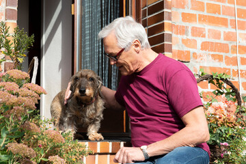 Mann sitzt mit Rauhaardackel am Hauseingang