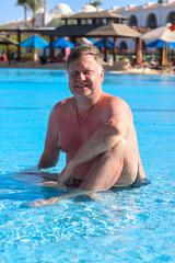 Relaxed Blond Man Enjoying Refreshing Dip in a Shallow Pool with Crystal Clear Water on a Sunny Day.