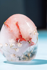 Frozen Easter egg with flowers in clear ice on blue background. High quality photo