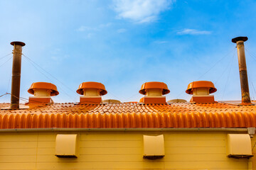 青空の下に並ぶオレンジ色の排気ファンと煙突