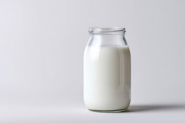 Glass jar filled with fresh milk against a neutral background