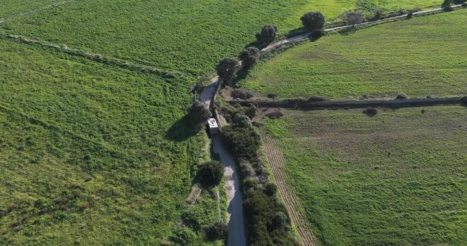 Aerial view of lush green fields intersected by a winding road with a vehicle, showcasing the rural landscape, Plemmirio, Sicily, Italy.