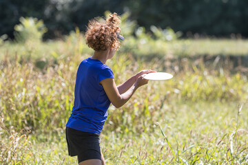 Female disc golf player throwing frisbee in sunny park, outdoor fitness recreation and sport training concept
