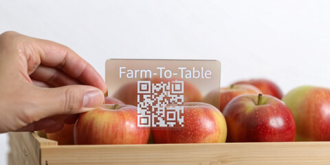 Farm to table concept with fresh apples in wooden crate and transparent card with QR code held by hand, promoting local food traceability