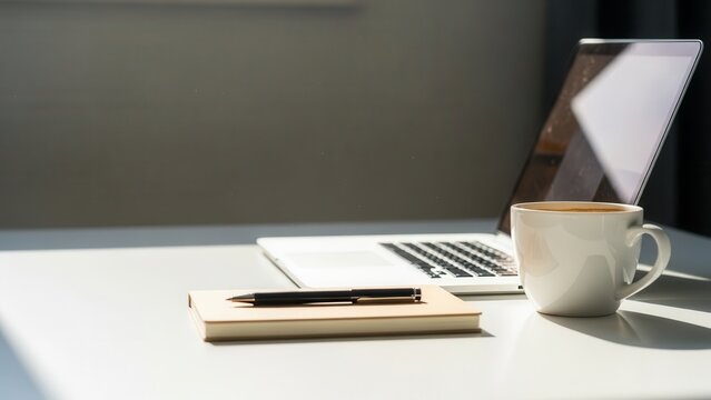 A modern laptop sits beside a coffee cup and notepad on a bright desk, ideal for remote work or business startup.