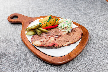 Beef brisket steak with baked potatoes. It is served in a white plate on a wooden cutting board....