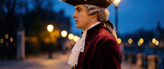 Elegant man in 18th-century Venetian costume with powdered wig and red velvet coat. Historical masquerade profile portrait at twilight during Carnival of Venice with city lights in background.
