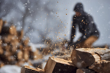 Cutting wood in snow with logs stacked in background during winter season