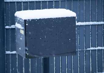Modern black metal mailbox covered in fresh winter snow on a matching fence