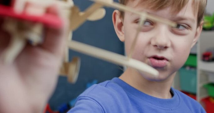 Happy schoolboy plays with plywood airplane model pretending flight in playroom closeup. Cute preteen kid holds vintage biplane made of wooden constructor set at home