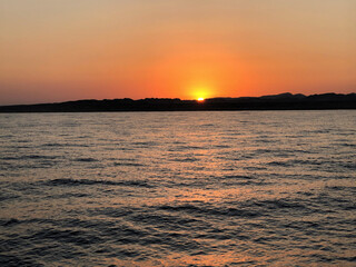 Naklejka premium Vibrant sunset over calm water with distant hills and orange sky