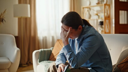 Displeased man sitting sofa living room with smartphone. Unhappy guy suffering