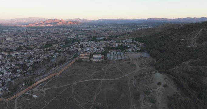 Drone aerial over Granada hillside trails at sunrise, city spreading into the distance with warm autumn light near the Alhambra, Andalusia Spain