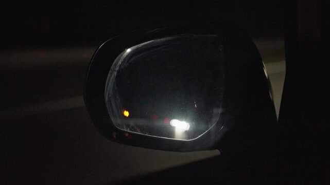 Night Side Mirror With Blinking Indicator And Approaching Headlights, Commuter Glances At Amber Safety Light, Closeup Reflection On Glass, Urban Road Glare And Cautious Atmosphere