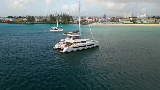 4K aerial drone half-circle orbit around catamaran at tropical beach in Barbados during afternoon