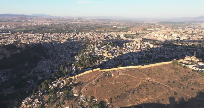 Aerial drone view of Granada and the Alhambra area at sunrise, long shadows over foothills and city blocks in crisp autumn light, Andalusia Spain