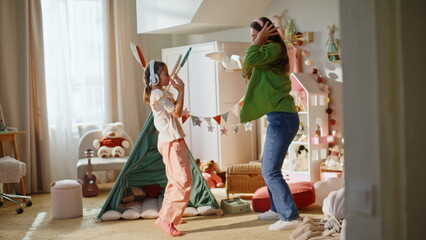 Mom child enjoying music at home. Overjoyed kid girl jumping at house with mommy