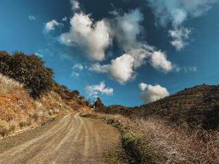 Upwards dirt road in Andalusian hilly landscape under blue sky with clouds.