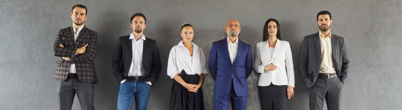 A diverse group of business people stand in a row against studio gray background, expressing unity and confidence for branding. Professional employees team posing for corporate portrait. 