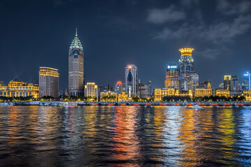 Naklejka premium Vibrant city skyline of the Bund at night in Shanghai, China with golden building reflections on the water.