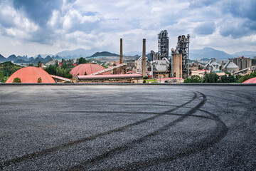 Obraz premium Industrial cement factory plant standing in a mountain landscape with an asphalt road and tire marks in the foreground.