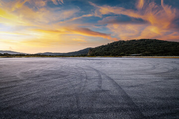 Dramatic empty asphalt ground with tire marks near a green mountain under a beautiful sunset sky. © zhao dongfang
