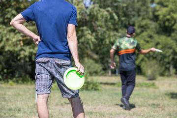 Disc golf player throwing frisbee in sunny park, outdoor fitness recreation and sport training concept