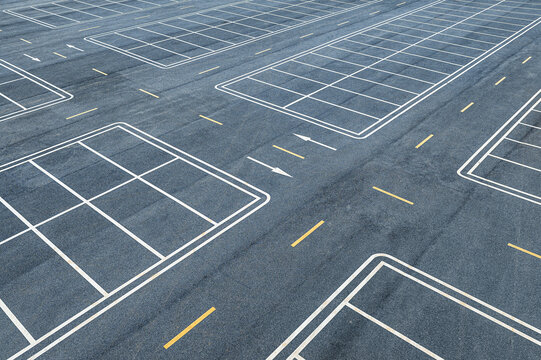 High angle view of an empty asphalt parking lot with white and yellow road markings in bright daylight.