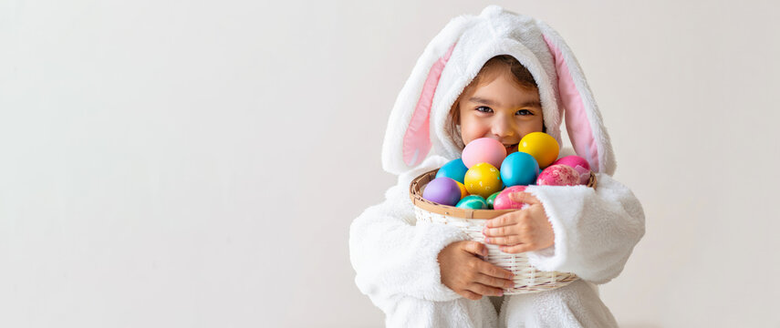 Cute Easter banner. Child in bunny costume holding colorful Easter eggs in basket on light background,  marketing materials, greeting cards, copy space, special offer, Easter sale, advertising