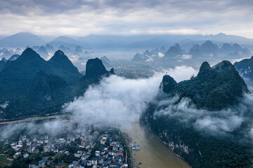 Majestic aerial view of the Li River winding through karst mountains and a village shrouded in morning mist in Guilin, China. © zhao dongfang